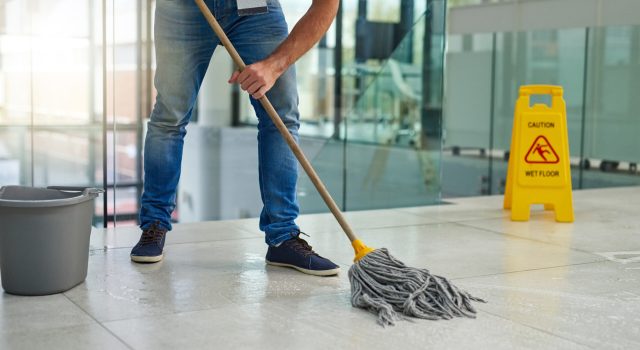 Shot of an unrecognizable man mopping the office floor.